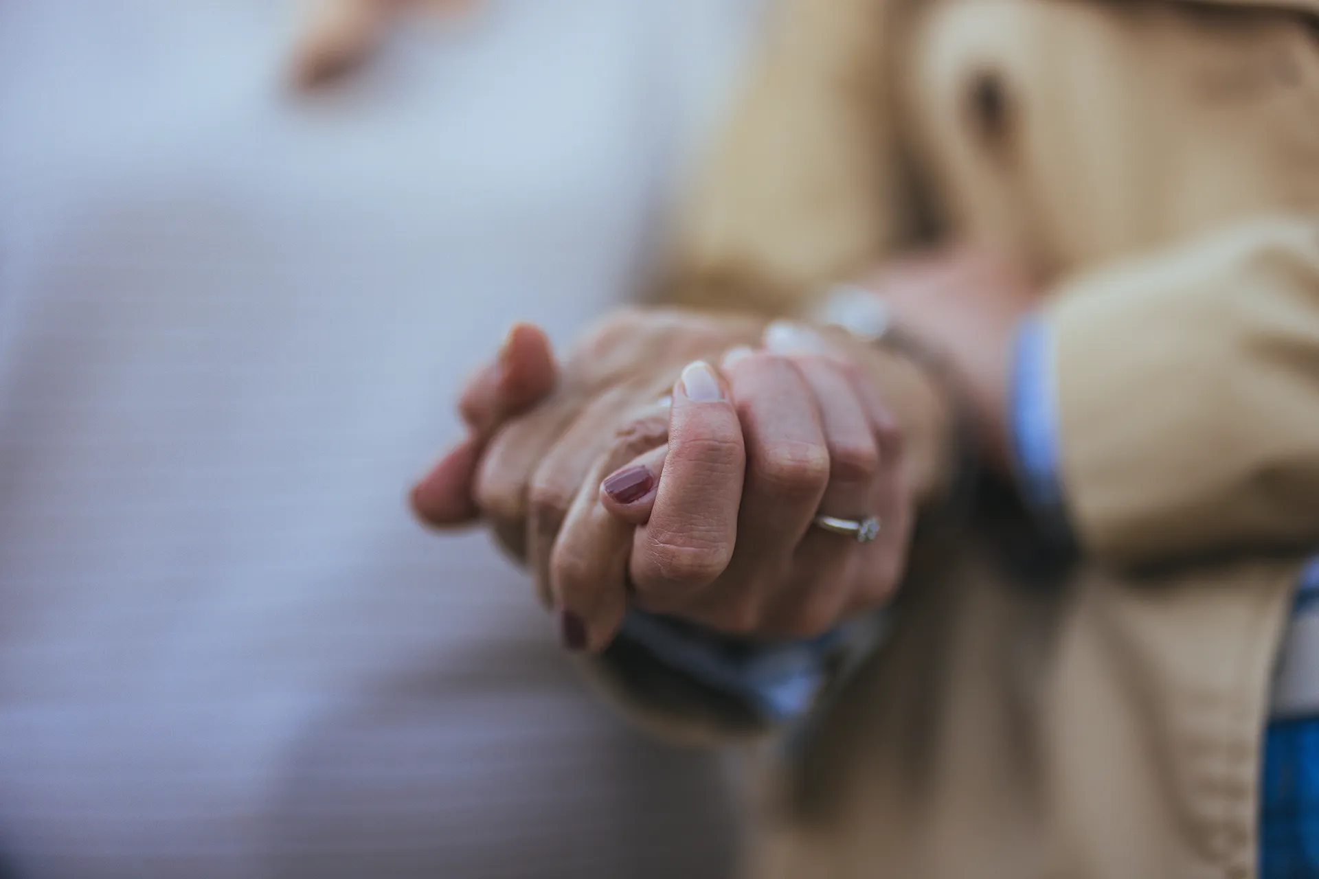 A close-up of a senior couple holding hands, with a wedding ring visible on the woman's finger, symbolizing love and commitment
