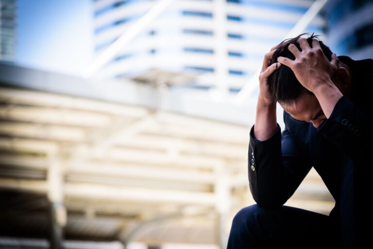 A stressed-out businessman puts his head in his hands while dealing with anxiety.