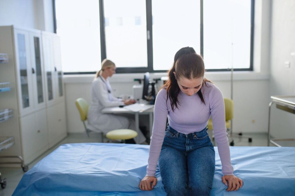 A teenage girl with POTS sitting on the exam bed during a doctor’s visit.