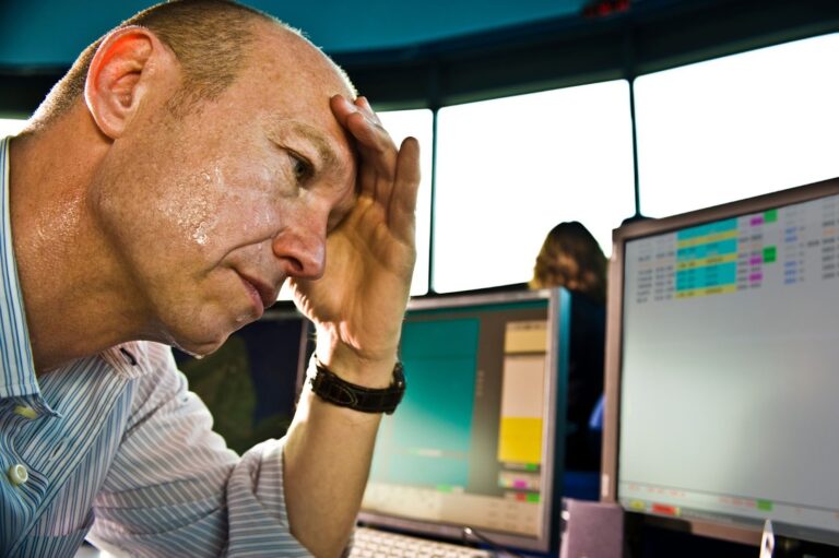 A male employee, experiencing mental fog, holds his forehead as he tries to focus on his work at his computer.